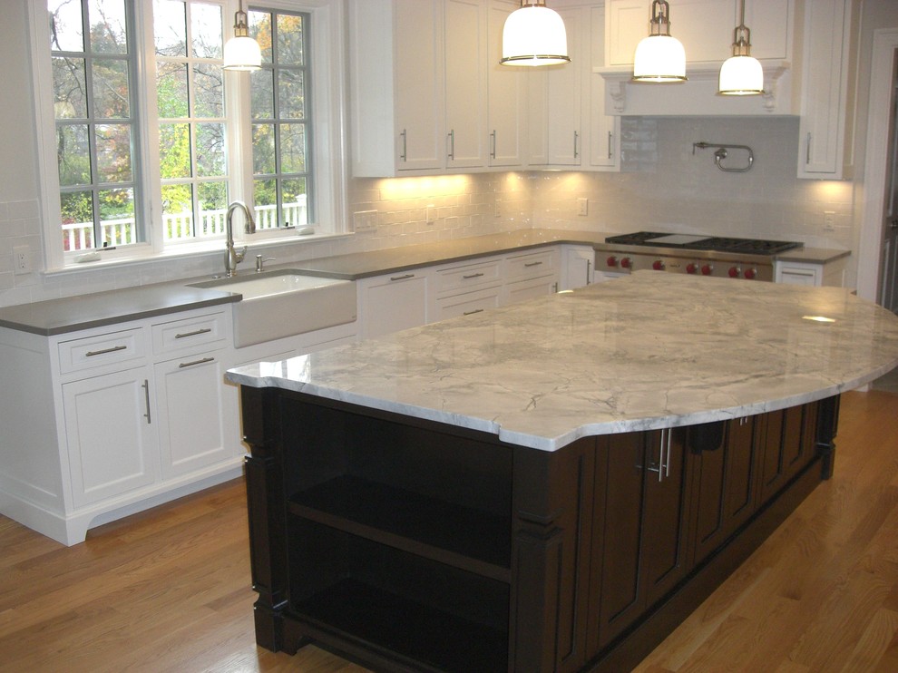 Inspiration for a large transitional u-shaped open plan kitchen in Boston with a farmhouse sink, shaker cabinets, white cabinets, granite benchtops, white splashback, subway tile splashback, stainless steel appliances, light hardwood floors, with island, beige floor and beige benchtop.