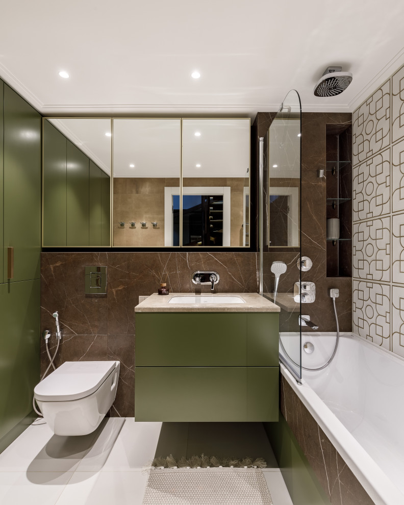 На фото: главная ванная комната среднего размера в стиле неоклассика (современная классика) с плоскими фасадами, зелеными фасадами, полновстраиваемой ванной, душем над ванной, инсталляцией, коричневой плиткой, керамогранитной плиткой, зелеными стенами, полом из керамогранита, врезной раковиной, столешницей из искусственного камня, бежевым полом, шторкой для ванной, бежевой столешницей, тумбой под одну раковину и подвесной тумбой