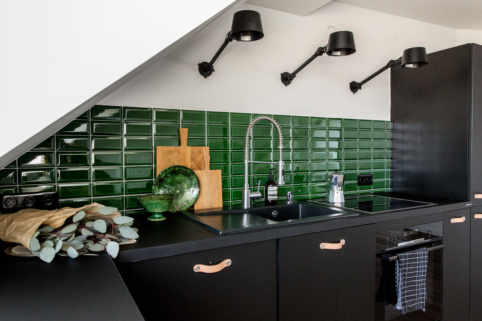 Inspiration for a contemporary l-shaped kitchen in Berlin with a drop-in sink, flat-panel cabinets, black cabinets, green splashback, subway tile splashback and black benchtop.