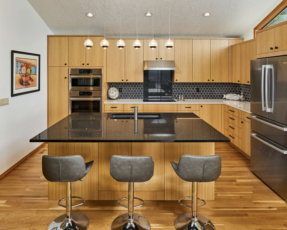 Photo of a large contemporary l-shaped open plan kitchen in Portland with an undermount sink, flat-panel cabinets, light wood cabinets, quartz benchtops, black splashback, porcelain splashback, stainless steel appliances, medium hardwood floors, with island, brown floor, multi-coloured benchtop and vaulted.