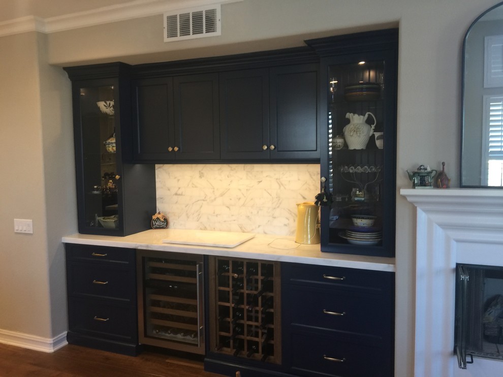 Large contemporary single-wall home bar in Los Angeles with no sink, shaker cabinets, white cabinets, solid surface benchtops, white splashback, marble splashback, dark hardwood floors, brown floor and white benchtop.