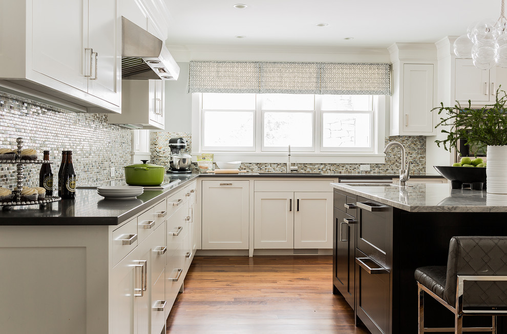 This is an example of a large transitional u-shaped open plan kitchen in Boston with an undermount sink, shaker cabinets, white cabinets, granite benchtops, metallic splashback, mosaic tile splashback, stainless steel appliances, medium hardwood floors, with island and brown floor.