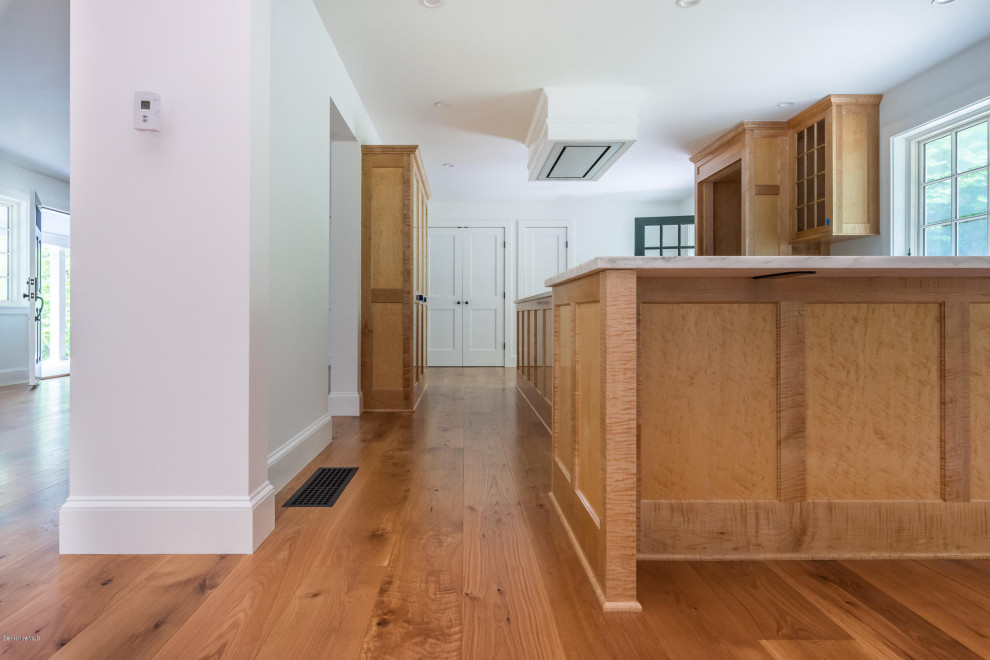 Example of a large transitional l-shaped medium tone wood floor and brown floor kitchen design with a farmhouse sink, light wood cabinets, marble countertops, white backsplash, marble backsplash, paneled appliances, an island and white countertops