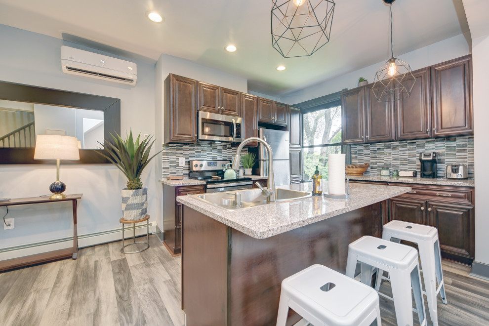 Example of a mid-sized transitional l-shaped gray floor open concept kitchen design with a double-bowl sink, raised-panel cabinets, dark wood cabinets, granite countertops, gray backsplash, matchstick tile backsplash, stainless steel appliances, an island and beige countertops