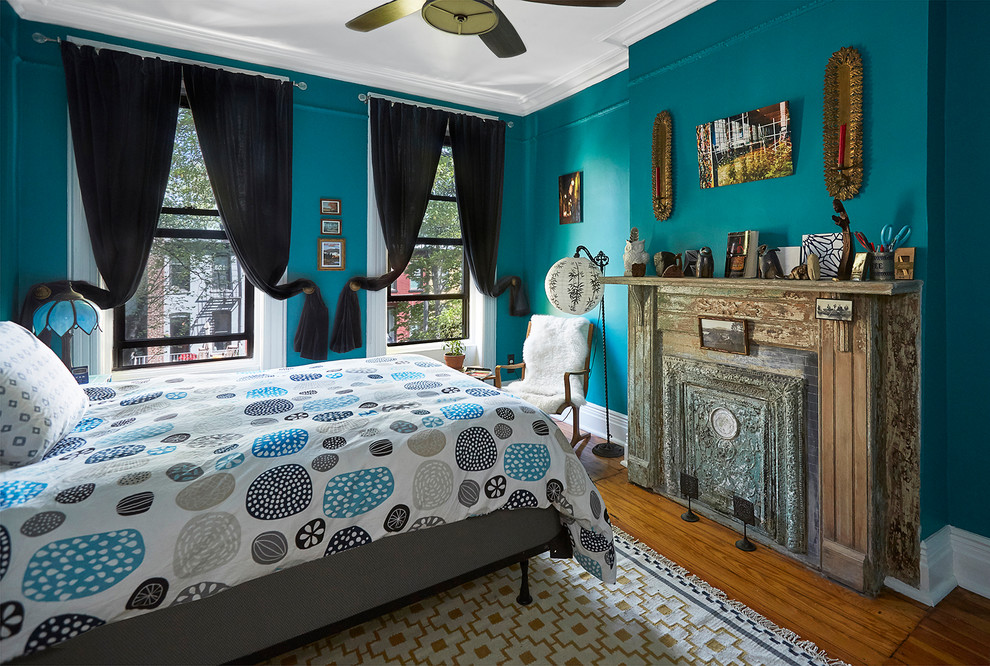 This is an example of a mid-sized eclectic master bedroom in New York with blue walls, medium hardwood floors, a hanging fireplace and a metal fireplace surround.