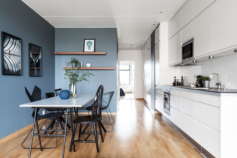 Design ideas for a mid-sized contemporary single-wall eat-in kitchen in Stockholm with flat-panel cabinets, white cabinets, white splashback, stainless steel appliances, medium hardwood floors, no island and a drop-in sink.