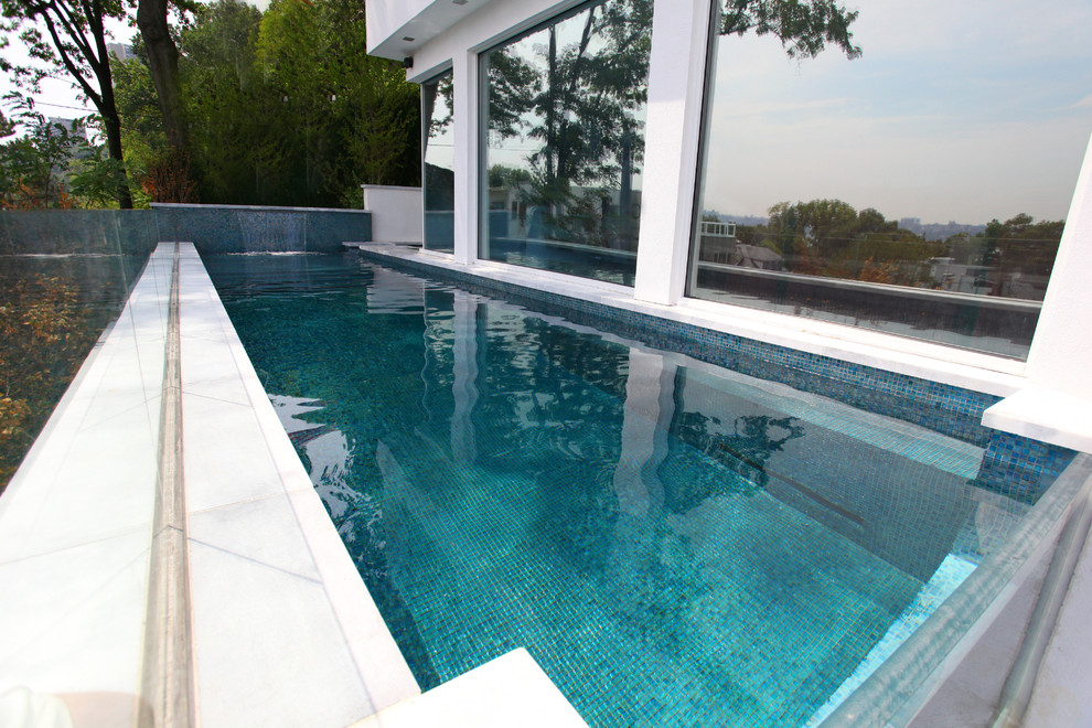 This is an example of a large modern side yard l-shaped lap pool in New York with a hot tub and concrete slab.