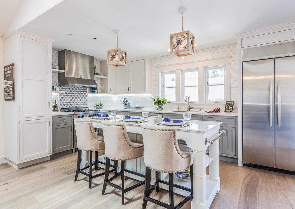 Photo of a beach style l-shaped kitchen in San Francisco with an undermount sink, recessed-panel cabinets, grey cabinets, white splashback, subway tile splashback, stainless steel appliances, medium hardwood floors and with island.