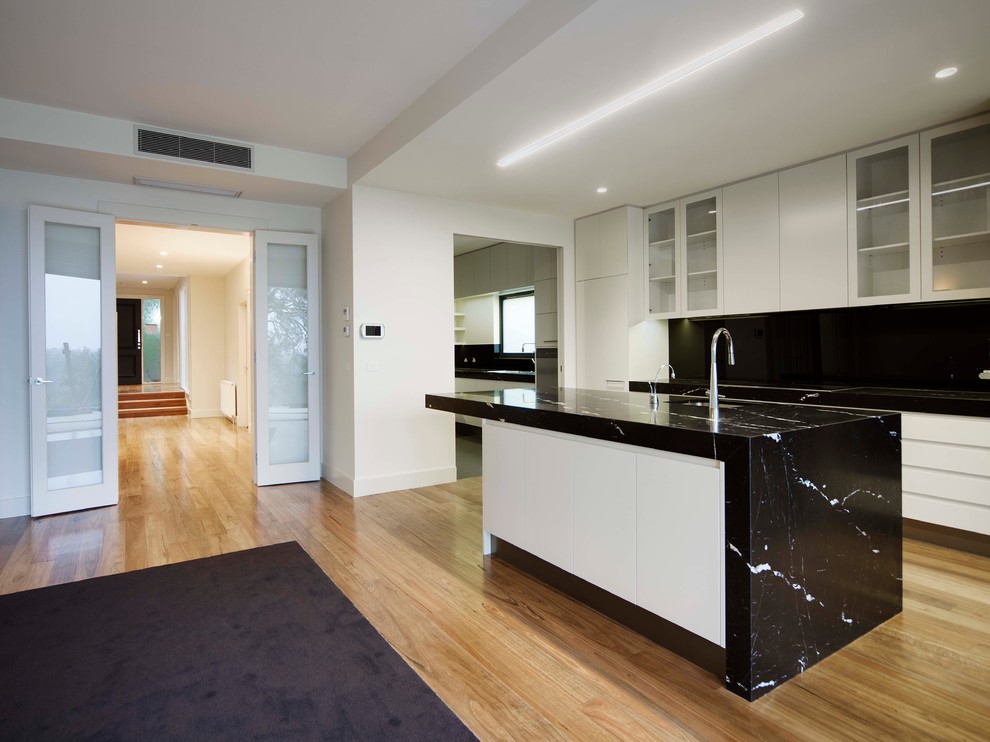 Design ideas for a large contemporary galley open plan kitchen in Melbourne with an undermount sink, flat-panel cabinets, white cabinets, marble benchtops, black splashback, glass sheet splashback, stainless steel appliances, light hardwood floors and multiple islands.