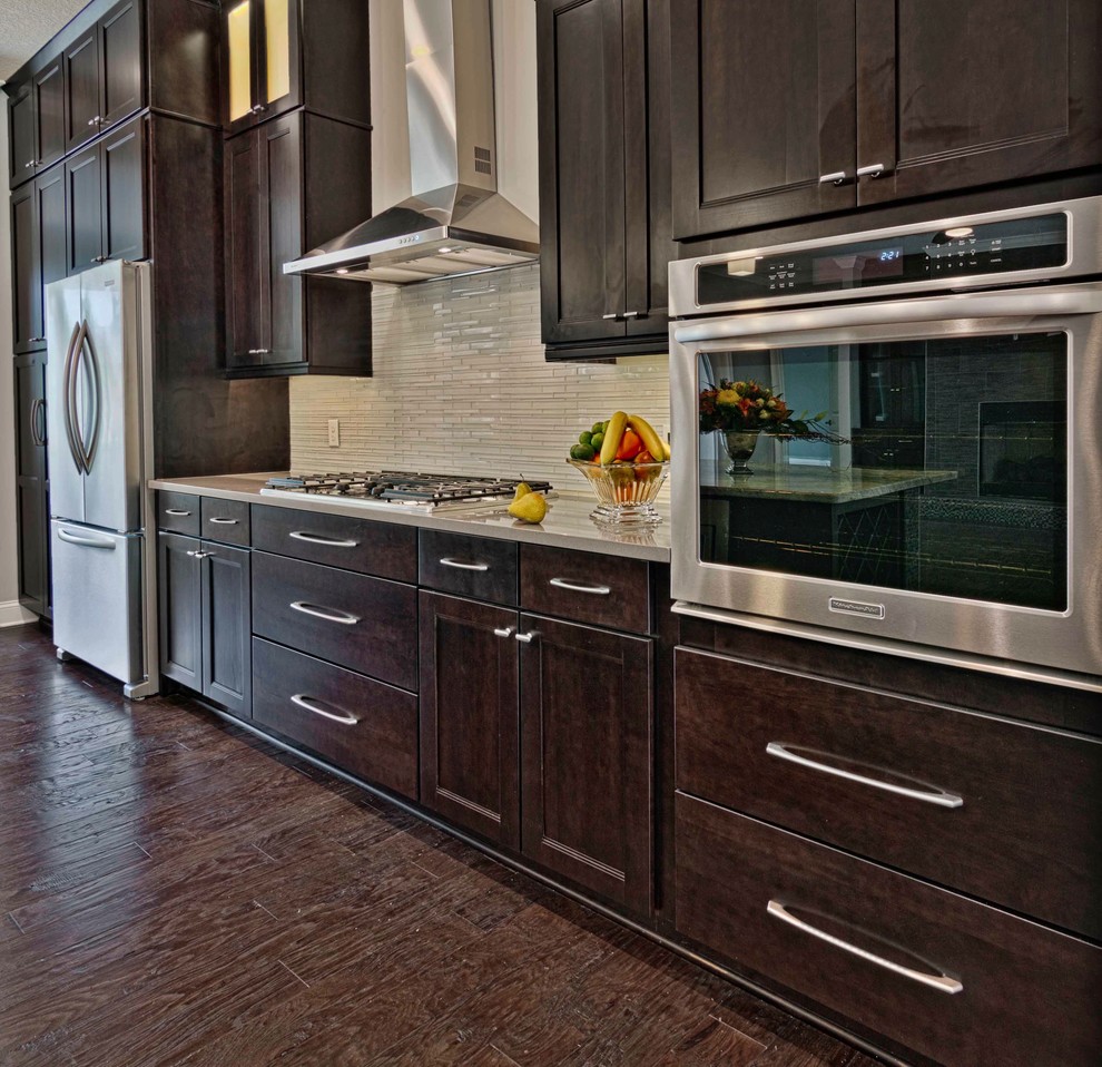 Inspiration for a traditional single-wall eat-in kitchen in Jacksonville with flat-panel cabinets, dark wood cabinets, granite benchtops, yellow splashback, glass tile splashback, stainless steel appliances, dark hardwood floors, with island, brown floor and grey benchtop.