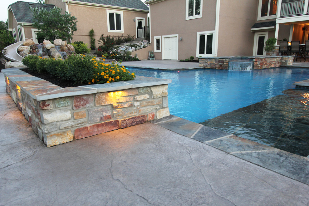This is an example of a large contemporary backyard l-shaped natural pool in Kansas City with stamped concrete and a water feature.