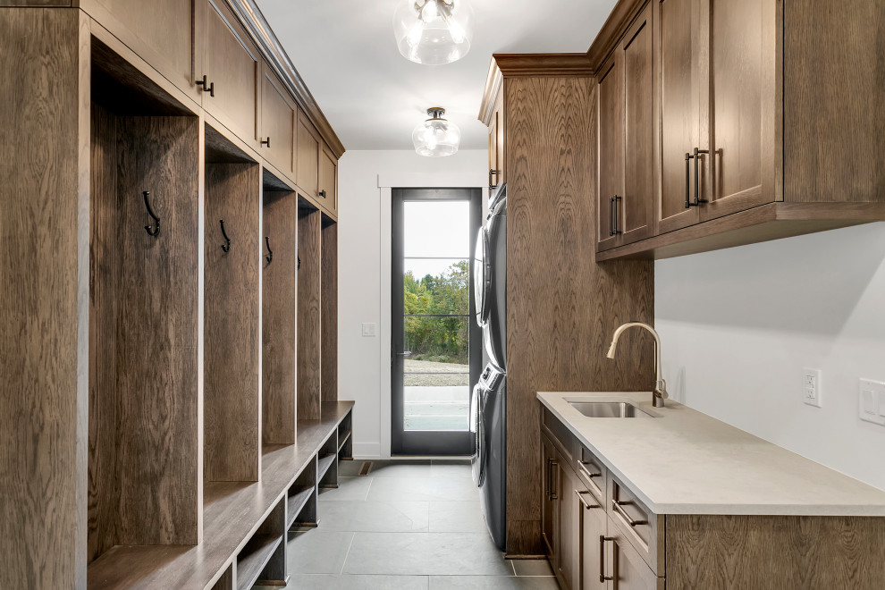 This is an example of a mid-sized country galley utility room in Other with an undermount sink, shaker cabinets, brown cabinets, soapstone benchtops, white walls, slate floors, a stacked washer and dryer, grey floor, beige benchtop and panelled walls.