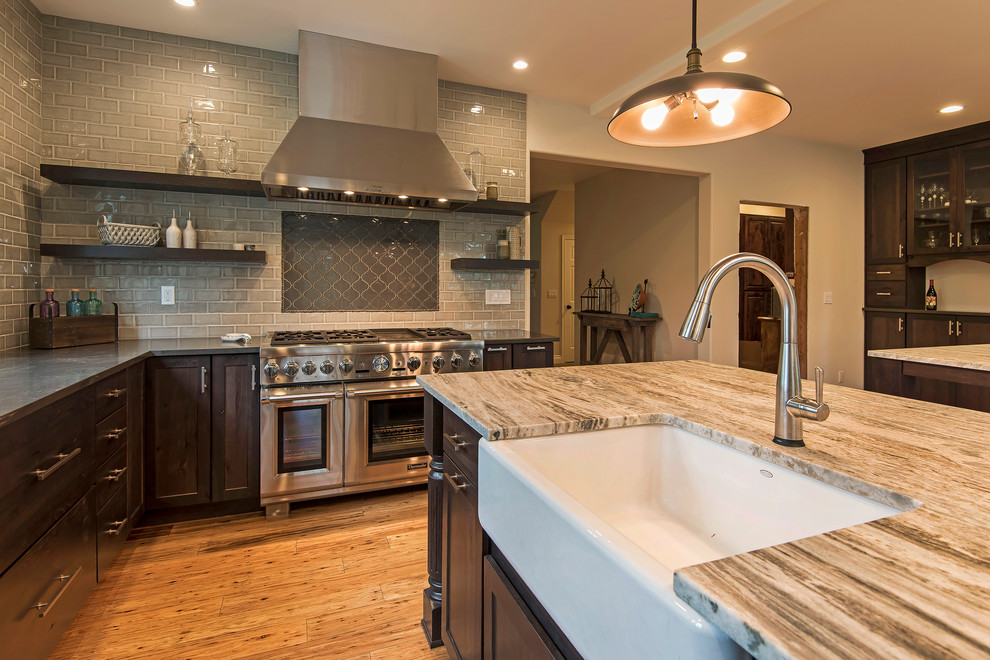 Example of a large transitional l-shaped medium tone wood floor and brown floor open concept kitchen design with a farmhouse sink, shaker cabinets, dark wood cabinets, granite countertops, gray backsplash, subway tile backsplash, paneled appliances and an island