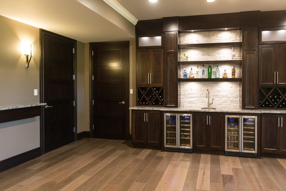 This is an example of an expansive contemporary single-wall wet bar in Chicago with an undermount sink, shaker cabinets, dark wood cabinets, granite benchtops, white splashback, stone tile splashback and light hardwood floors.