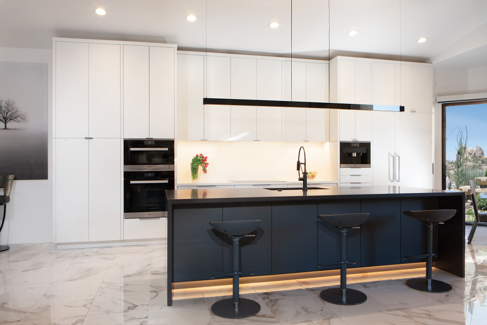 Inspiration for a contemporary galley eat-in kitchen in Phoenix with flat-panel cabinets, white cabinets, with island, an undermount sink, white splashback, panelled appliances, multi-coloured floor and black benchtop.