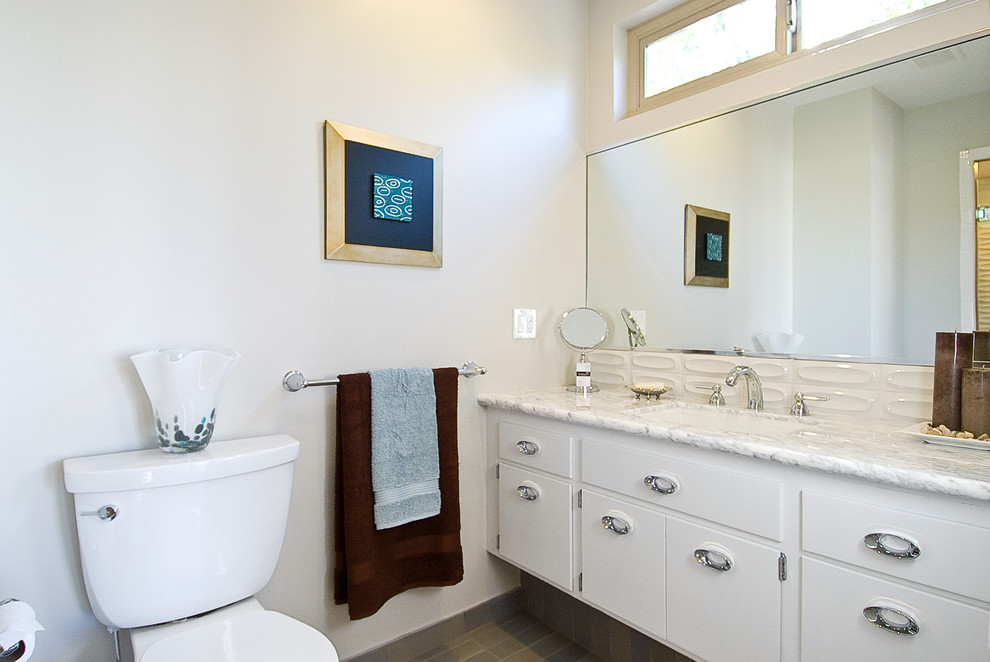 This is an example of a midcentury bathroom in San Francisco with flat-panel cabinets, white cabinets, a drop-in tub, an alcove shower, a two-piece toilet, beige tile, ceramic tile, white walls, ceramic floors, a drop-in sink and marble benchtops.