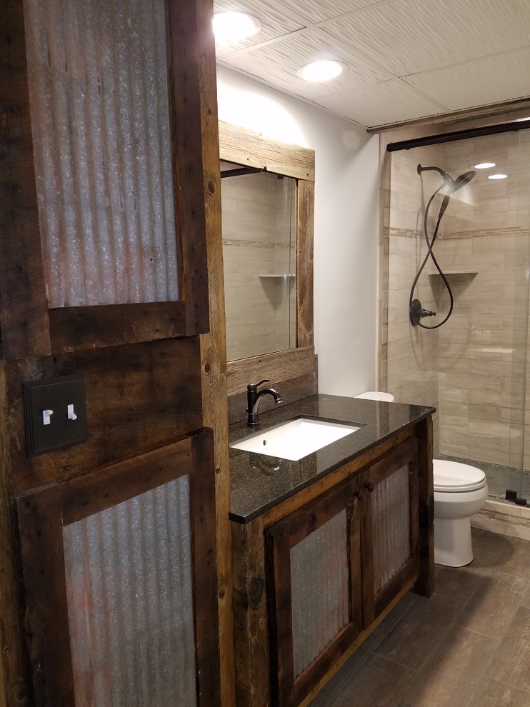 Inspiration for a mid-sized country 3/4 bathroom in Minneapolis with louvered cabinets, dark wood cabinets, an alcove shower, a two-piece toilet, beige tile, stone tile, grey walls, medium hardwood floors, an undermount sink, engineered quartz benchtops, brown floor and a sliding shower screen.