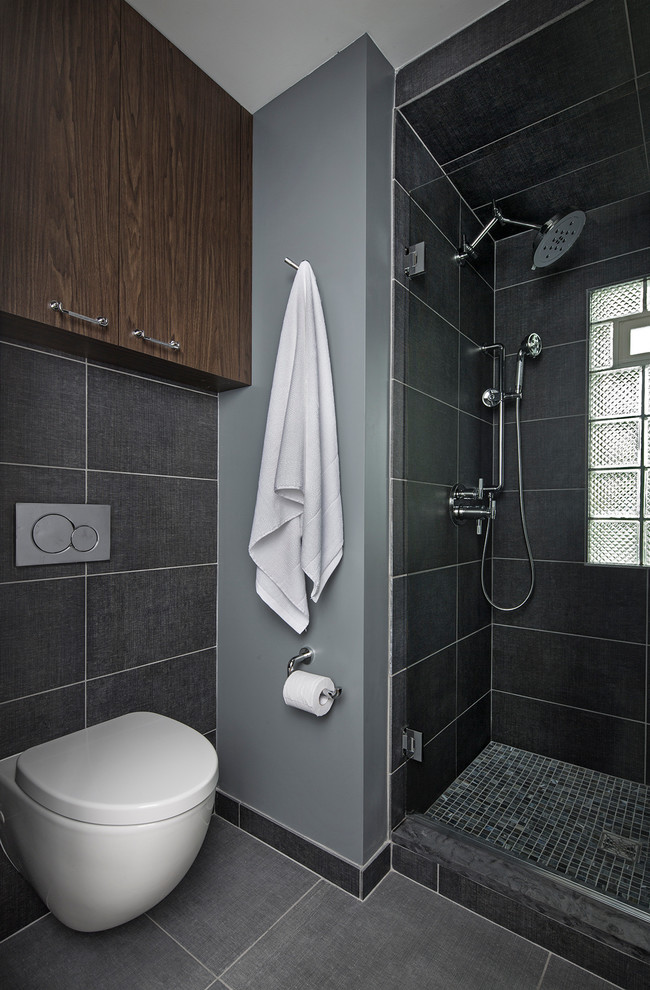 This is an example of a small industrial 3/4 bathroom in Detroit with flat-panel cabinets, medium wood cabinets, an alcove shower, a wall-mount toilet, blue tile, porcelain tile, blue walls, porcelain floors, an undermount sink, granite benchtops, blue floor, a hinged shower door and black benchtops.