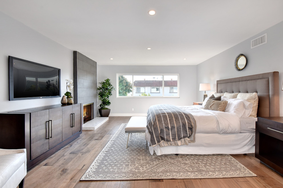 Inspiration for a transitional bedroom in Orange County with grey walls, medium hardwood floors, a standard fireplace, a tile fireplace surround and brown floor.