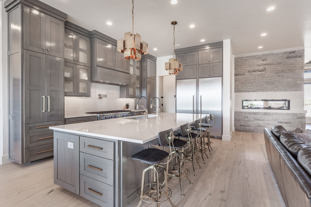 Design ideas for a transitional l-shaped open plan kitchen in Oklahoma City with an undermount sink, shaker cabinets, grey cabinets, white splashback, stainless steel appliances, light hardwood floors, with island and beige floor.