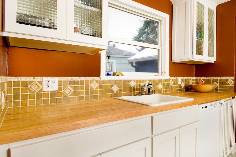 Enclosed kitchen - large transitional l-shaped enclosed kitchen idea in Seattle with a single-bowl sink, glass-front cabinets, white cabinets, wood countertops, white backsplash, ceramic backsplash, stainless steel appliances, brown walls and no island