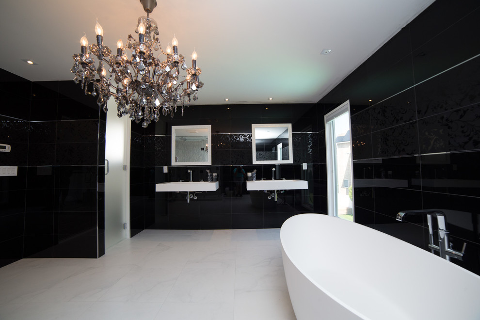 This is an example of a large modern bathroom in New York with an integrated sink, open cabinets, white cabinets, engineered quartz benchtops, a freestanding tub, a corner shower, a one-piece toilet, black tile, glass sheet wall, black walls and concrete floors.