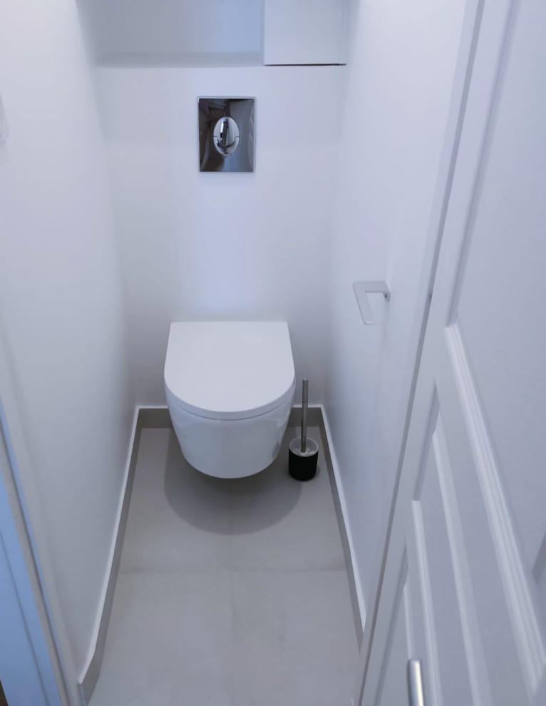Exempel på ett litet klassiskt toalett, med släta luckor, vita skåp, en vägghängd toalettstol, vita väggar och grått golv