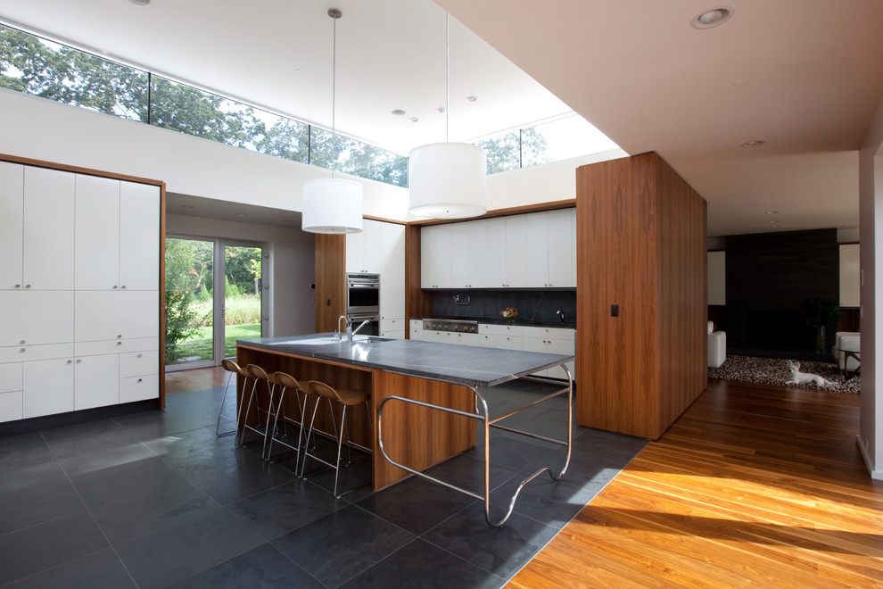 Design ideas for a modern u-shaped open plan kitchen in Other with soapstone benchtops, an undermount sink, flat-panel cabinets, white cabinets, black splashback, stainless steel appliances and slate floors.