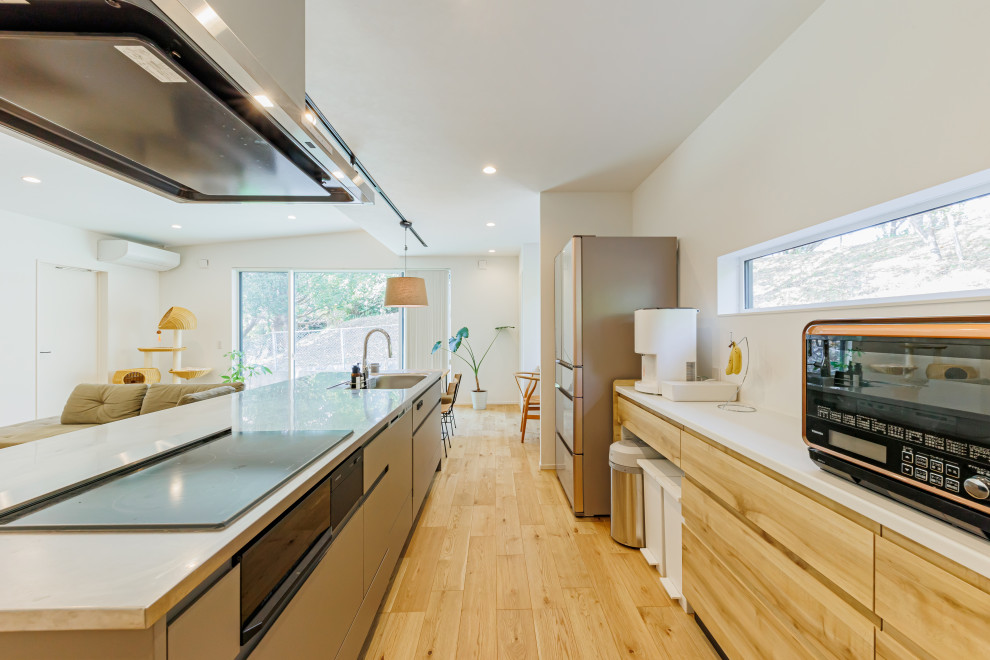 Mid-sized modern galley open plan kitchen in Kobe with an integrated sink, grey splashback, medium hardwood floors, beige floor, white benchtop and wallpaper.