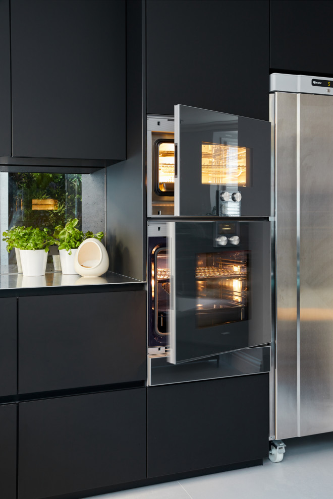 Photo of a small modern single-wall eat-in kitchen in London with flat-panel cabinets, black cabinets, stainless steel benchtops and with island.