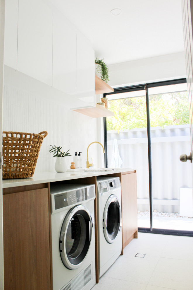 This is an example of a mid-sized country single-wall dedicated laundry room in Perth with a farmhouse sink, flat-panel cabinets, dark wood cabinets, quartz benchtops, white walls, porcelain floors, a side-by-side washer and dryer, multi-coloured floor and white benchtop.