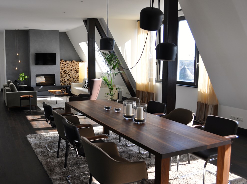 Photo of a large industrial dining room in Berlin with white walls, dark hardwood floors, a wood stove, a plaster fireplace surround and brown floor.