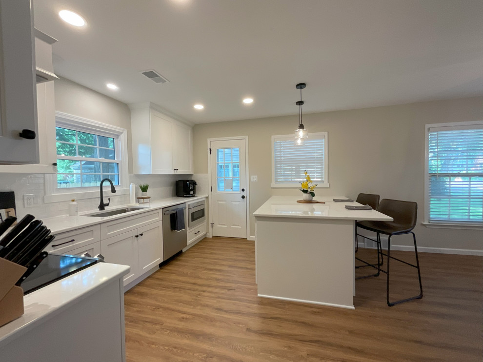 Design ideas for a small transitional l-shaped eat-in kitchen in Detroit with an undermount sink, shaker cabinets, white cabinets, quartz benchtops, white splashback, ceramic splashback, stainless steel appliances, medium hardwood floors, with island, brown floor and white benchtop.