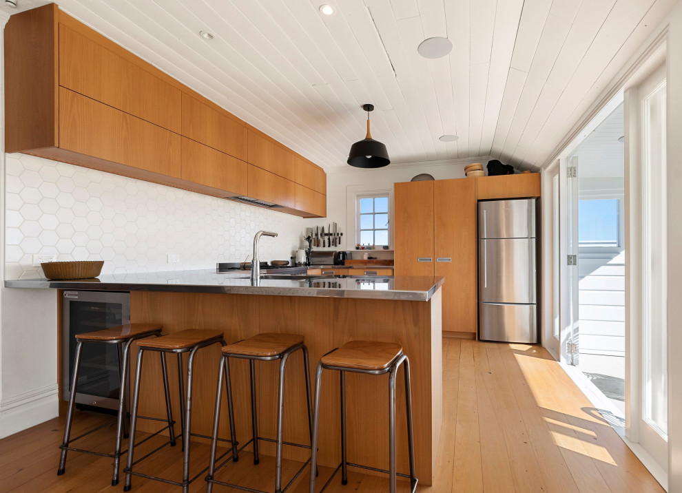 Mid-sized modern u-shaped eat-in kitchen in Auckland with a single-bowl sink, flat-panel cabinets, medium wood cabinets, stainless steel benchtops, stainless steel appliances, medium hardwood floors, no island, brown floor and timber.