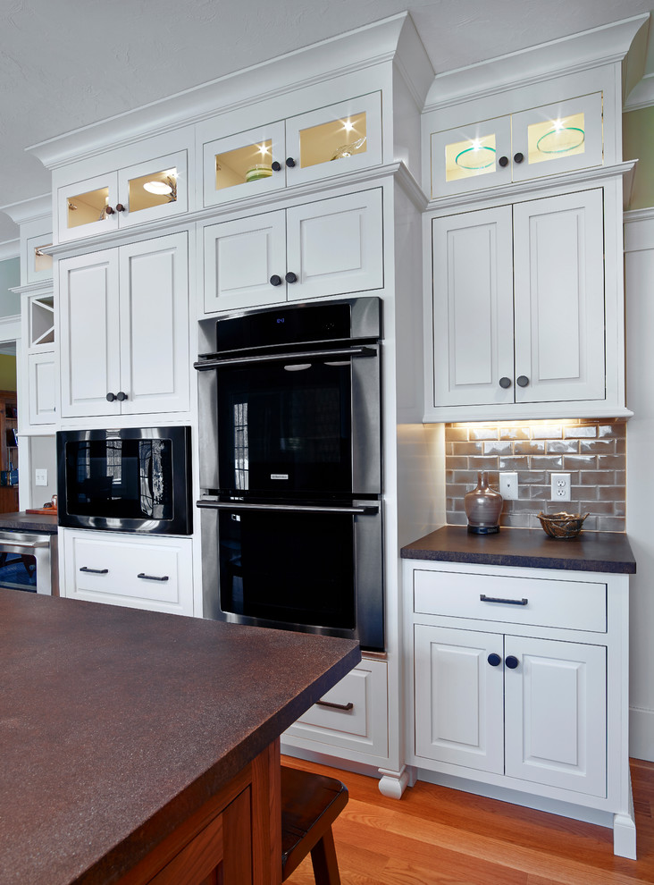 Enclosed kitchen - mid-sized transitional u-shaped medium tone wood floor and brown floor enclosed kitchen idea in Providence with a farmhouse sink, raised-panel cabinets, white cabinets, gray backsplash, subway tile backsplash, stainless steel appliances and an island