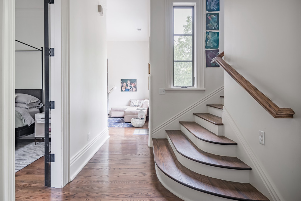 Imagen de escalera curva clásica grande con escalones de madera, contrahuellas de madera y barandilla de madera