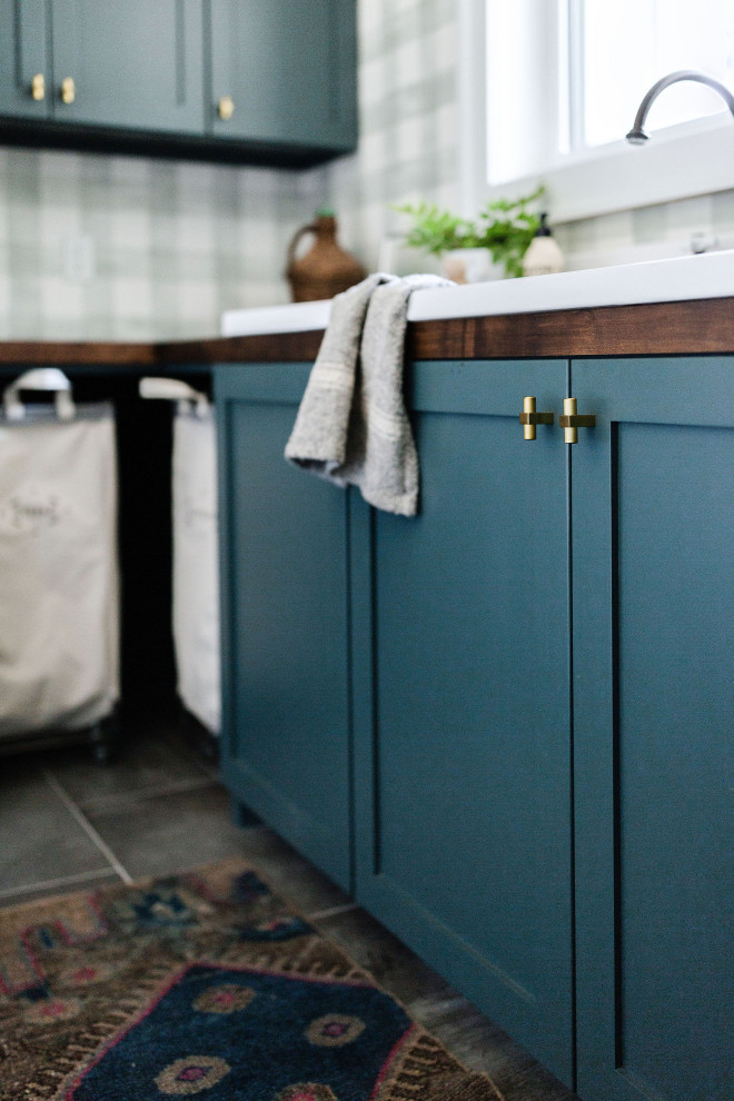 Foto på en lantlig bruna tvättstuga, med en rustik diskho, skåp i shakerstil, gröna skåp, träbänkskiva, vita väggar, klinkergolv i keramik, en tvättmaskin och torktumlare bredvid varandra och grått golv
