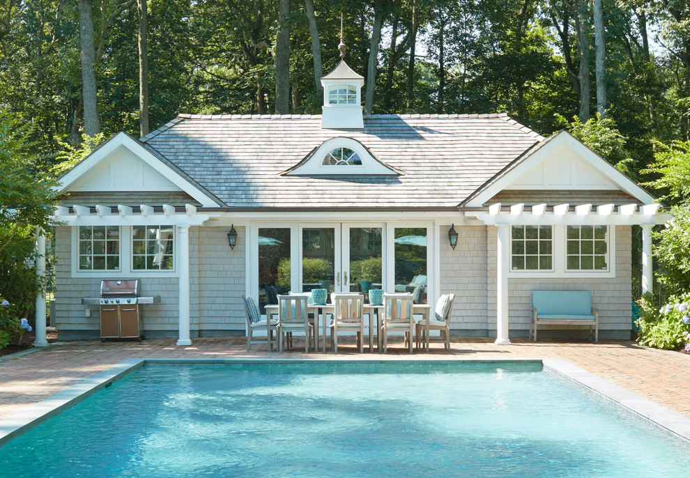 Traditional rectangular pool in Other with a pool house and brick pavers.