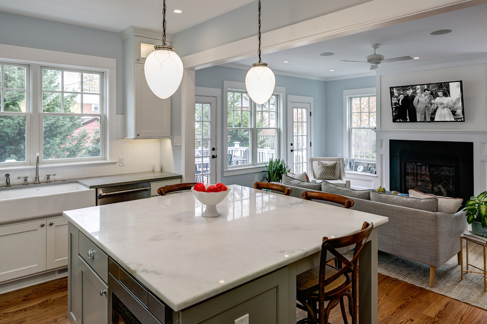 This is an example of a mid-sized arts and crafts l-shaped eat-in kitchen in Orange County with a farmhouse sink, shaker cabinets, white cabinets, marble benchtops, white splashback, subway tile splashback, stainless steel appliances, medium hardwood floors and with island.