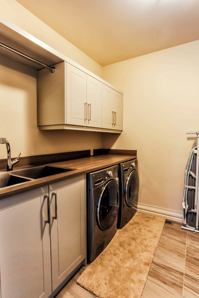 Mid-sized country single-wall dedicated laundry room in Calgary with a double-bowl sink, shaker cabinets, grey cabinets, laminate benchtops, beige walls, porcelain floors and a side-by-side washer and dryer.