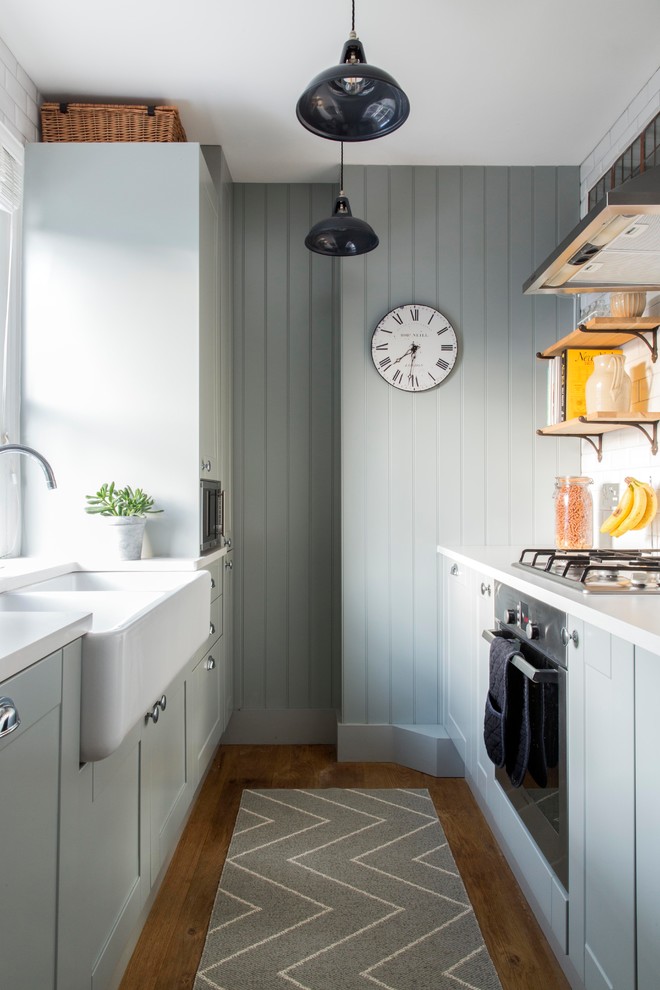 This is an example of a transitional galley kitchen in London with a farmhouse sink, shaker cabinets, grey cabinets, medium hardwood floors and brown floor.