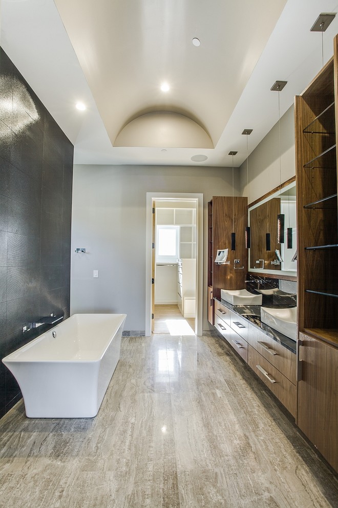 Photo of a mid-sized contemporary master bathroom in Dallas with flat-panel cabinets, medium wood cabinets, a freestanding tub, a wall-mount toilet, gray tile, ceramic tile, grey walls, ceramic floors, a vessel sink and granite benchtops.