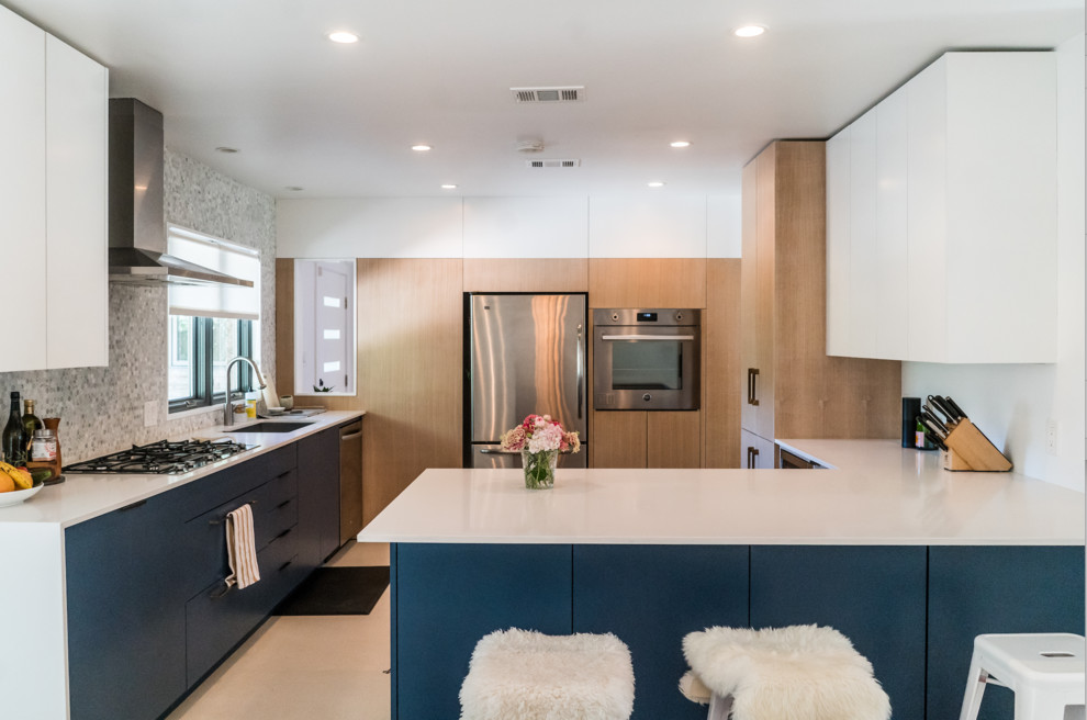 This is an example of a modern single-wall separate kitchen in Austin with an undermount sink, flat-panel cabinets, blue cabinets, grey splashback, mosaic tile splashback, stainless steel appliances, a peninsula and beige floor.