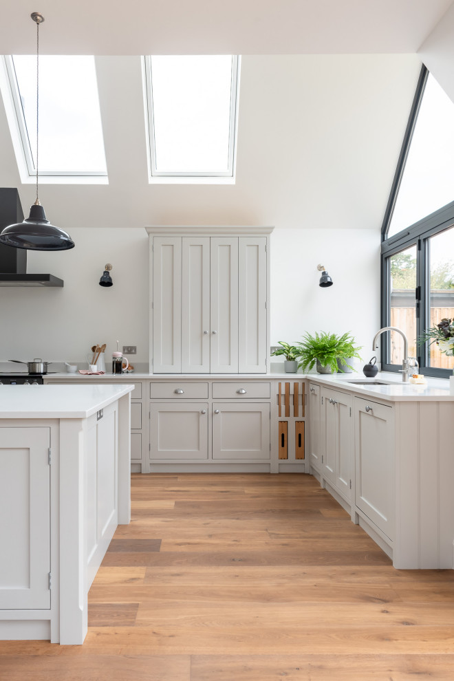 Inspiration for a large traditional u-shaped open plan kitchen in Surrey with shaker cabinets, white cabinets, quartzite benchtops, black appliances, light hardwood floors, with island, brown floor and white benchtop.