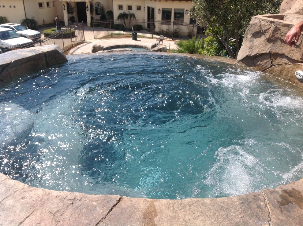 Photo of a large beach style backyard custom-shaped natural pool in Los Angeles with a water feature and natural stone pavers.