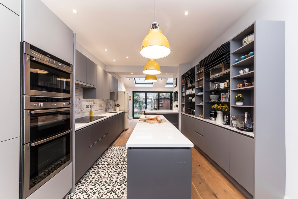 Photo of a mid-sized contemporary eat-in kitchen in London with an undermount sink, flat-panel cabinets, grey cabinets, solid surface benchtops, multi-coloured splashback, glass sheet splashback, stainless steel appliances, medium hardwood floors and with island.