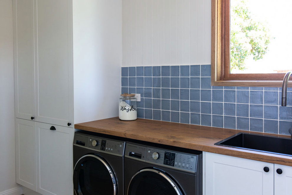 Photo of a large country galley utility room in Melbourne with a single-bowl sink, shaker cabinets, white cabinets, laminate benchtops, blue splashback, ceramic splashback, white walls, a side-by-side washer and dryer and decorative wall panelling.