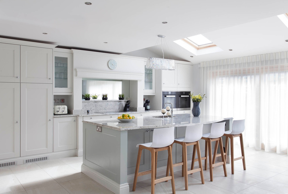 Large transitional l-shaped open plan kitchen in Dublin with an integrated sink, shaker cabinets, blue cabinets, granite benchtops, multi-coloured splashback, stone slab splashback, black appliances, ceramic floors and with island.
