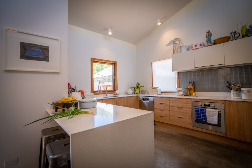 Design ideas for a mid-sized country u-shaped eat-in kitchen in Other with light wood cabinets, grey splashback, stainless steel appliances, concrete floors, grey floor and white benchtop.