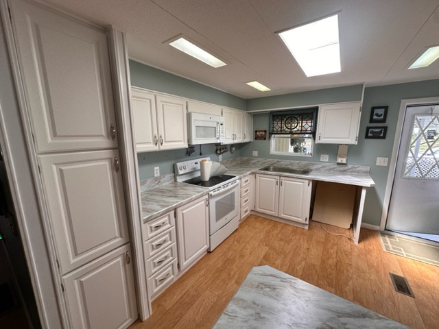 Mid-sized l-shaped eat-in kitchen photo with raised-panel cabinets, white cabinets, laminate countertops, white backsplash and white countertops